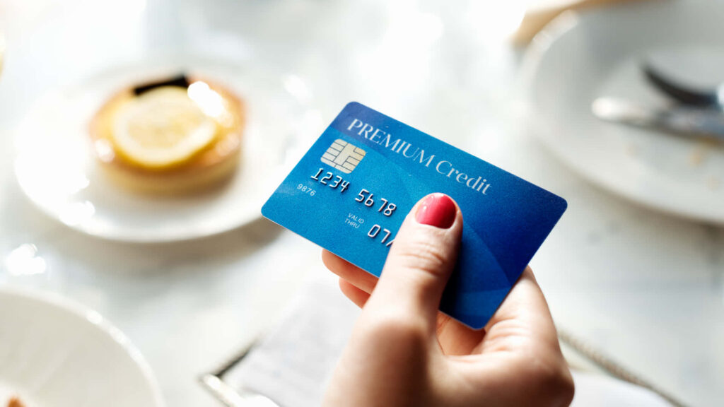 Woman holding blue premium credit card over table with food in soft daylight lifestyle scene Wallpaper