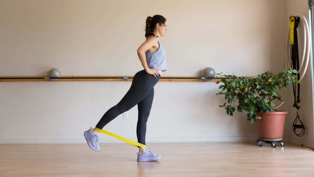Woman doing standing leg exercise with yellow resistance band in bright modern fitness studio Wallpaper