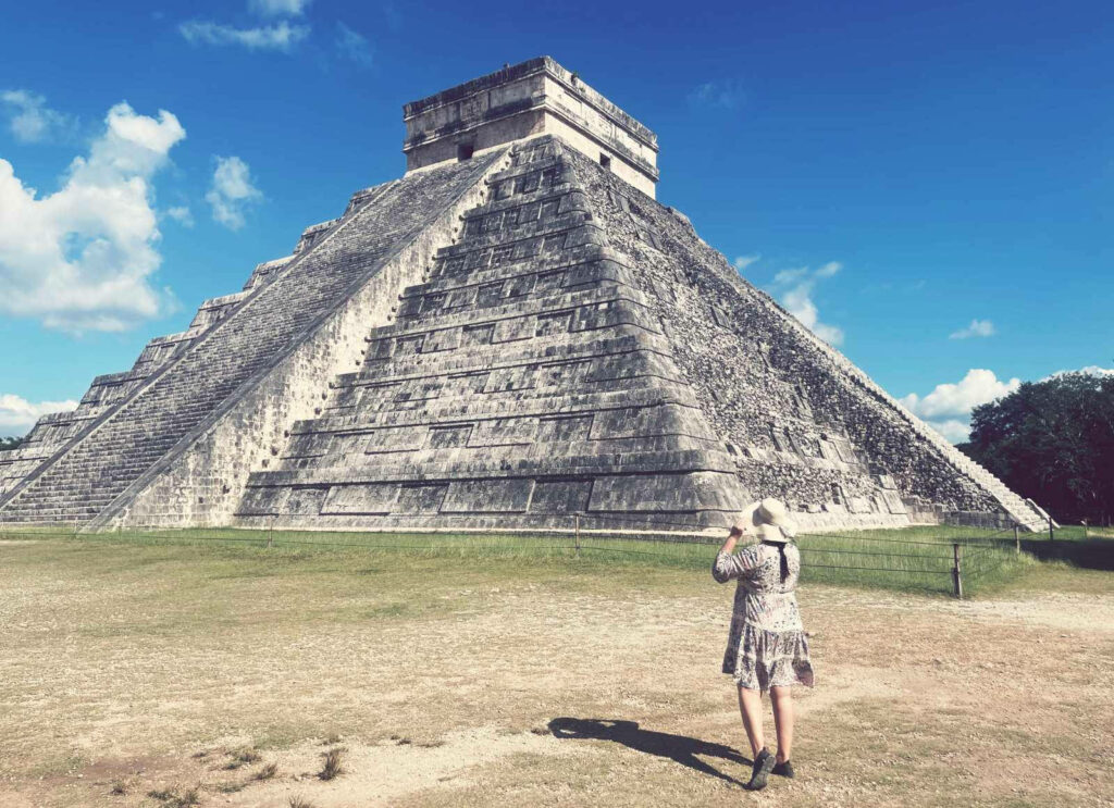 Woman standing before Chichen Itza pyramid with stone steps under vivid blue sky wallpaper background
