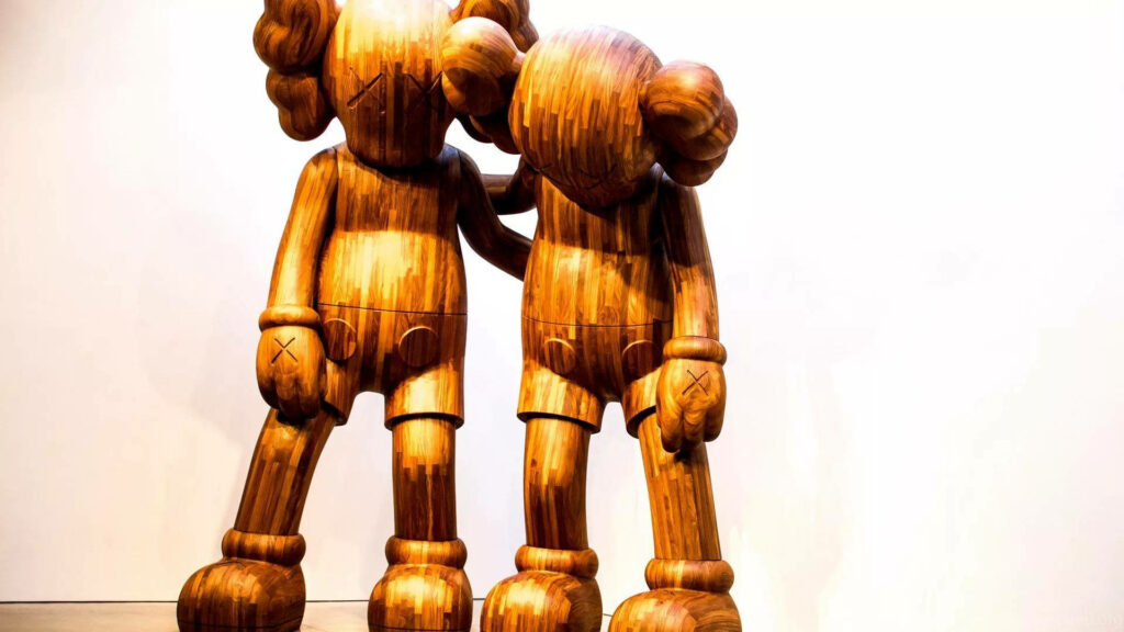 Wooden KAWS Along The Way figures side by side with one consoling the other on bright background Wallpaper