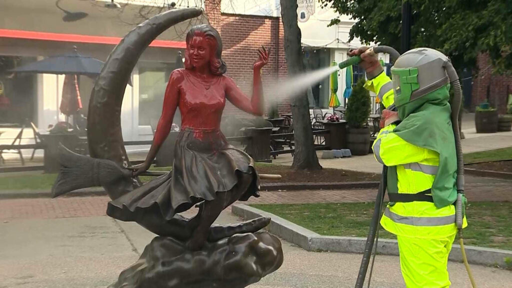 Worker in protective gear cleaning Bewitched Samantha Stephens statue on crescent moon outdoors Wallpaper