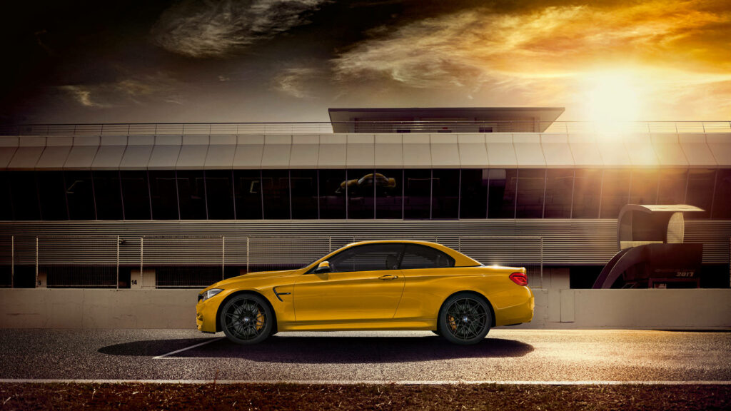 Yellow BMW M4 parked by modern building under warm dramatic sunset sky wallpaper background