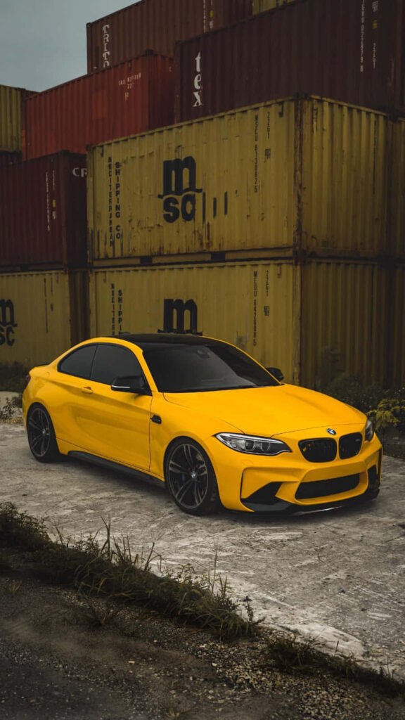 Yellow BMW parked by red and yellow cargo containers vibrant industrial wallpaper background