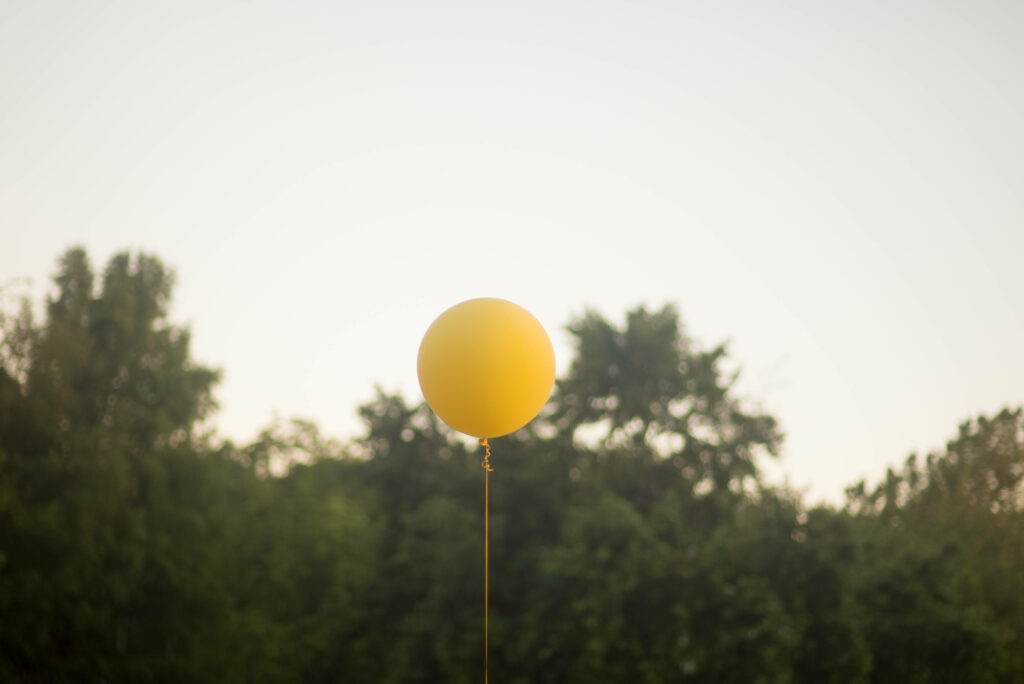 Yellow balloon floating above green trees under clear sky peaceful uplifting wallpaper background
