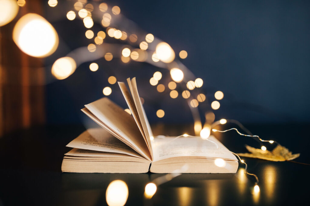 Open book with glowing fairy lights and golden bokeh on dark cozy background HD wallpaper