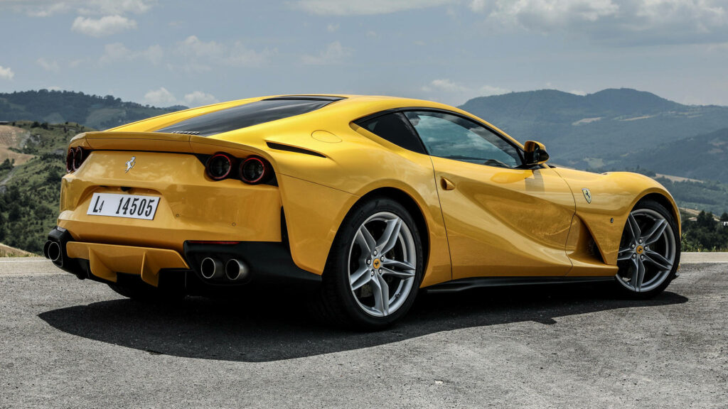 Rear view of yellow Ferrari 812 Superfast on mountain road with rolling hills scenic background Wallpaper