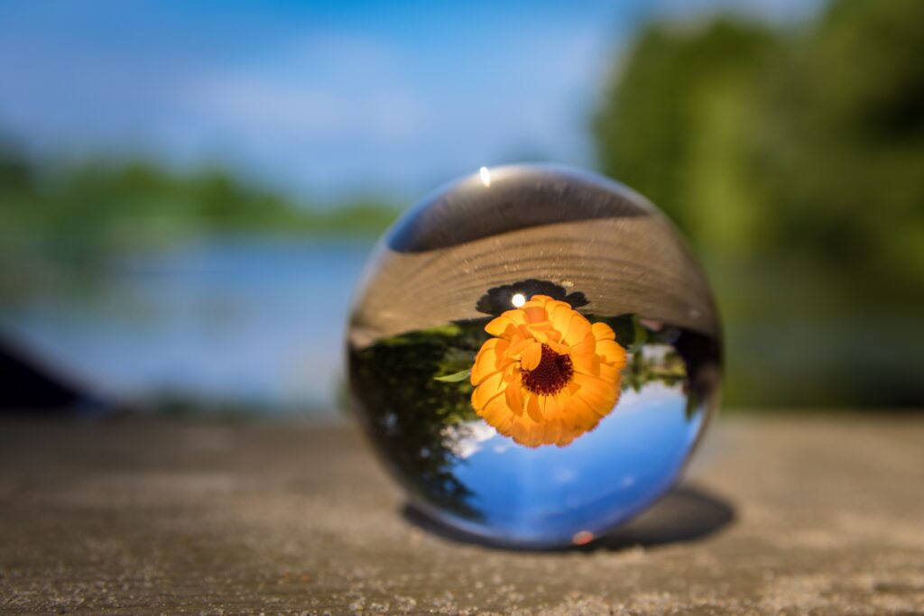 Crystal lensball with inverted yellow flower on concrete with blue sky bokeh background macro photo Wallpaper