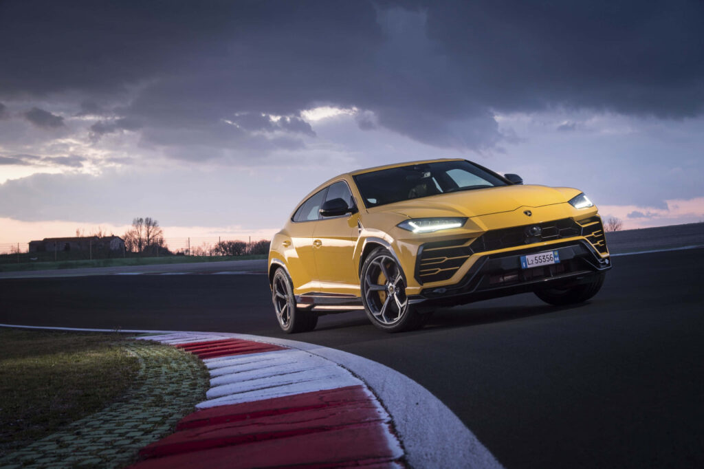 Yellow Lamborghini Urus SUV speeding on racetrack under cloudy sky showcasing sporty design Wallpaper