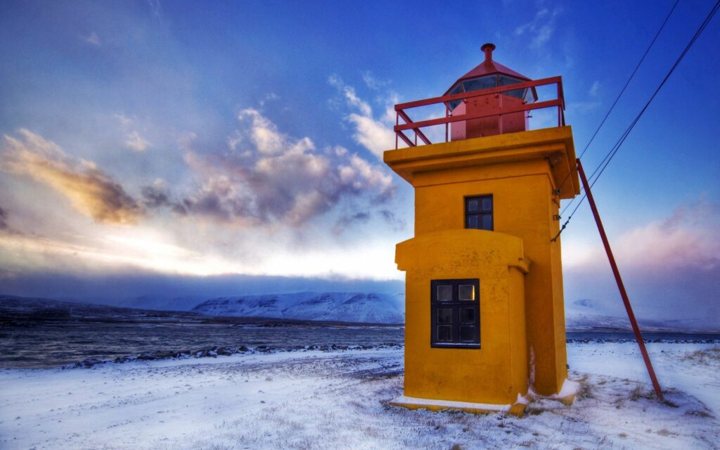 Bright yellow lighthouse with taut wires amid snowy winter landscape under vivid blue sky Wallpaper
