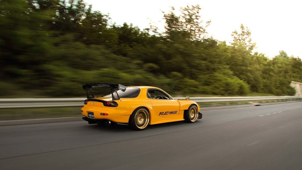 Yellow Mazda RX-7 FD with RE Amemiya widebody and gold wheels speeding in dynamic JDM wallpaper