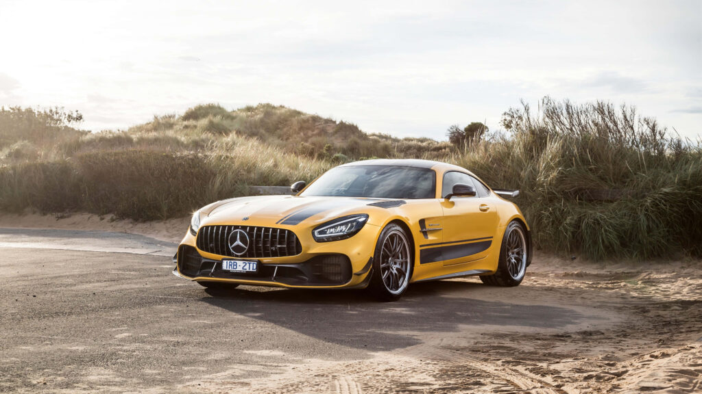 Yellow Mercedes AMG GT R parked on coastal road with grassy dunes highlighting sporty design Wallpaper