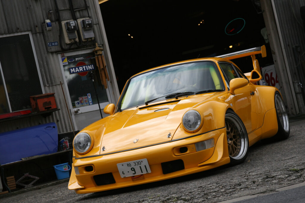 Yellow Porsche 911 Turbo: Classic Power Against Martini Racing Garage Wallpaper