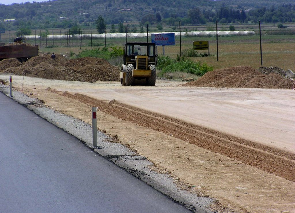 Yellow road roller compacting soil near new asphalt road on rural construction site landscape Wallpaper