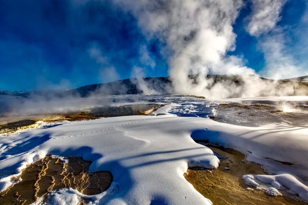 Steaming Yellowstone geyser in snowy winter landscape under vivid blue sky wallpaper background