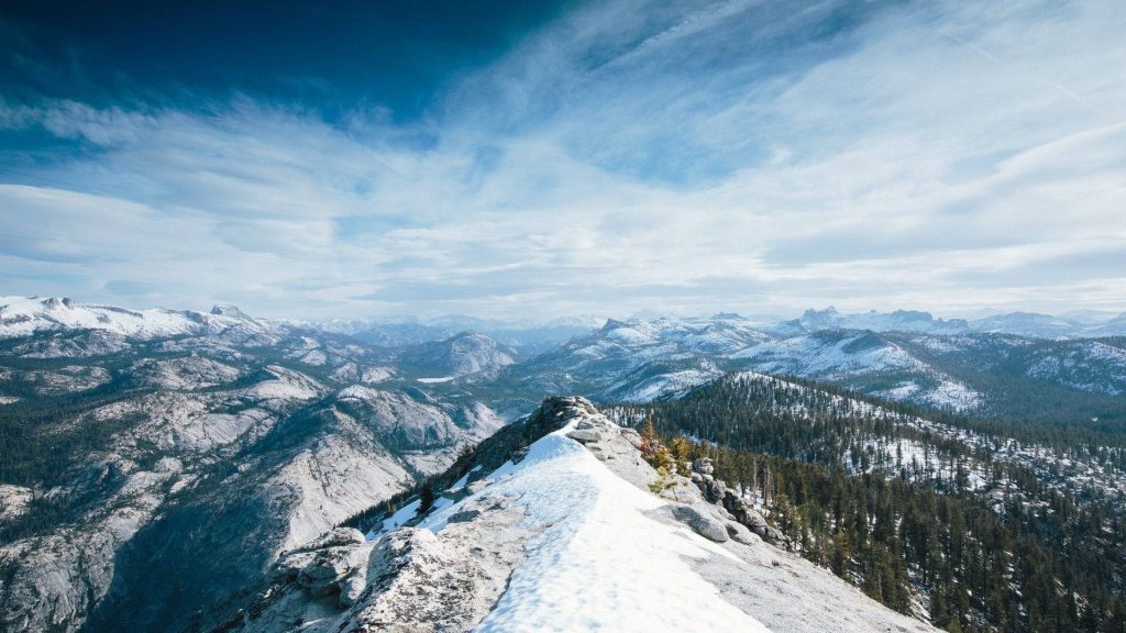 Snow-dusted granite ridge and evergreen forests under blue sky in Yosemite National Park Wallpaper