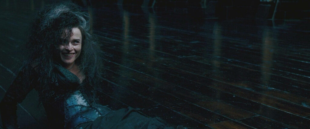 Young Bellatrix Lestrange sitting on dark floor wild hair mischievous smile intense personality wallpaper