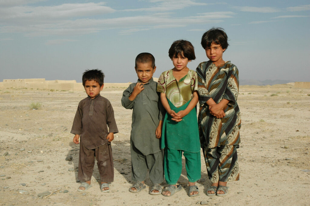 Young Afghan boys in traditional clothing view rugged rural Afghanistan landscape under open sky Wallpaper