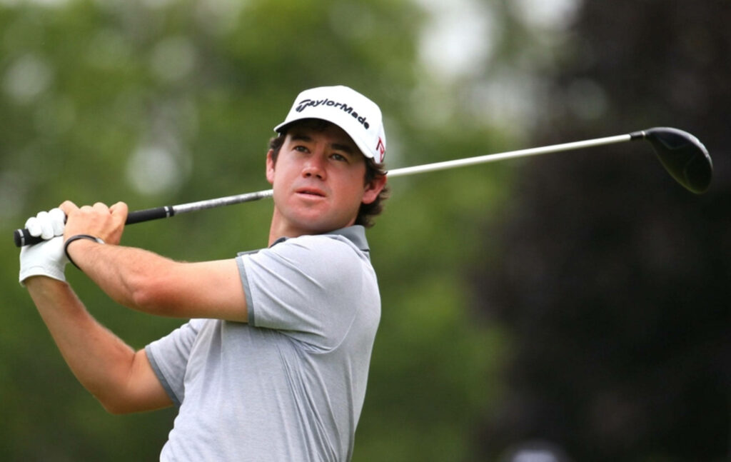 Young Brian Harman mid-swing on green golf course wearing grey polo and white Taylormade cap Wallpaper