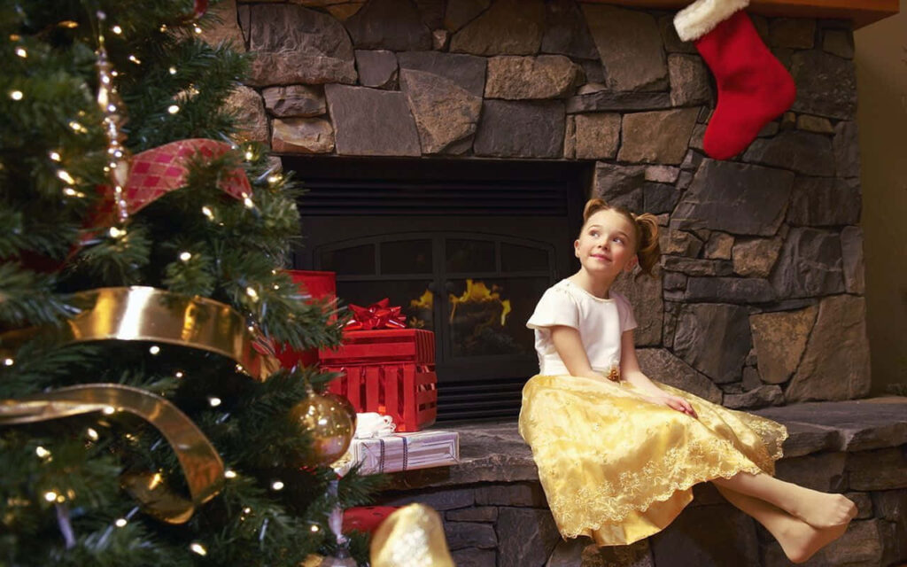 Cozy Holiday Scene: Girl by Festive Fireplace and Decorated Tree Wallpaper