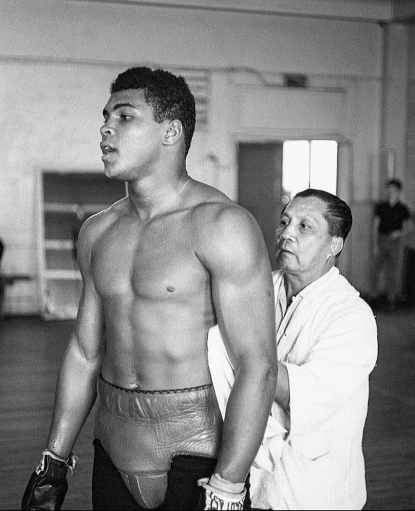 Black and white image of young Muhammad Ali training in Clay boxing shorts with gym attendant Wallpaper