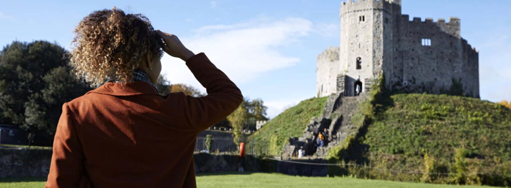Young woman on green grass admiring Cardiff Castle autumn medieval architecture blue sky Wallpaper
