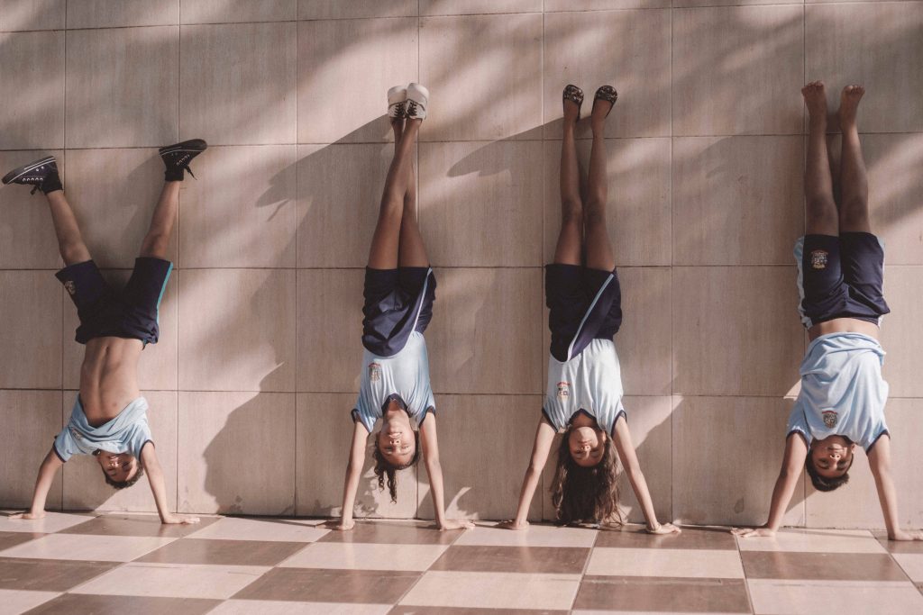 Four children in school uniforms doing synchronized handstands on geometric tiled floor Wallpaper