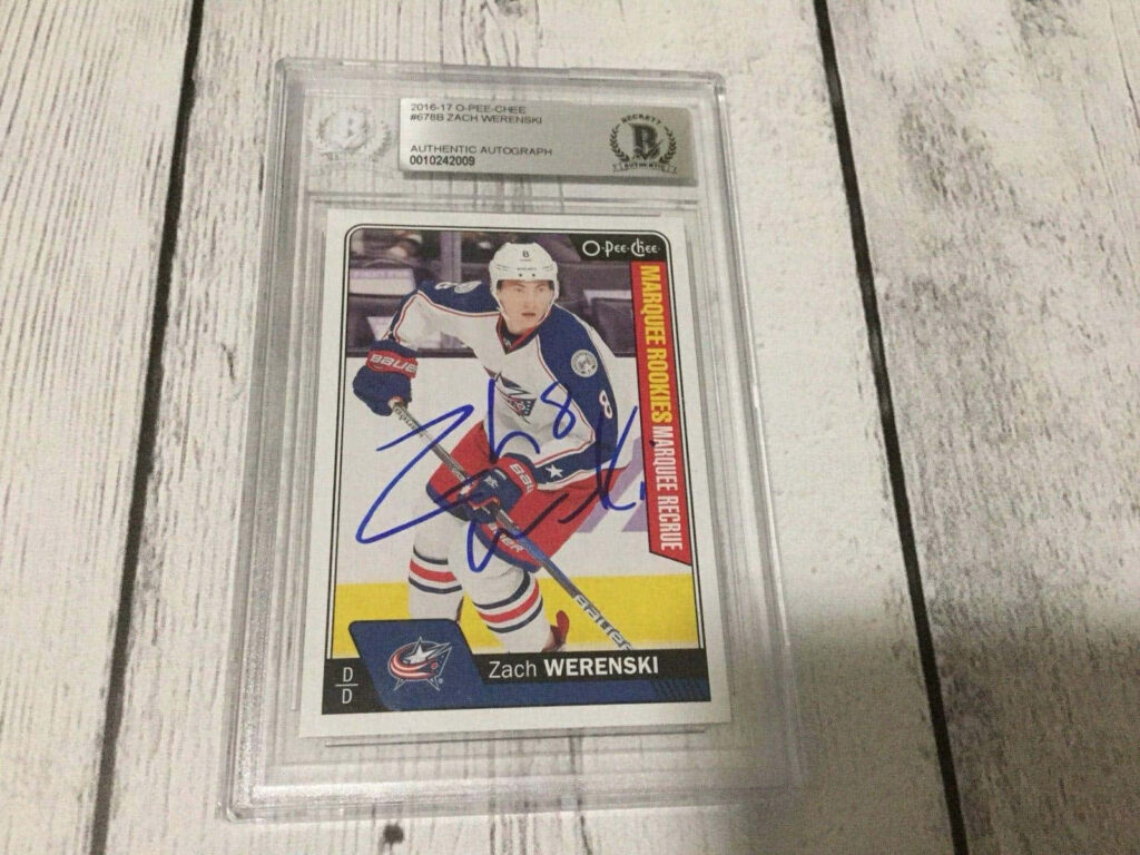 Signed Zachary Werenski hockey rookie card in Blue Jackets uniform on light wooden background Wallpaper