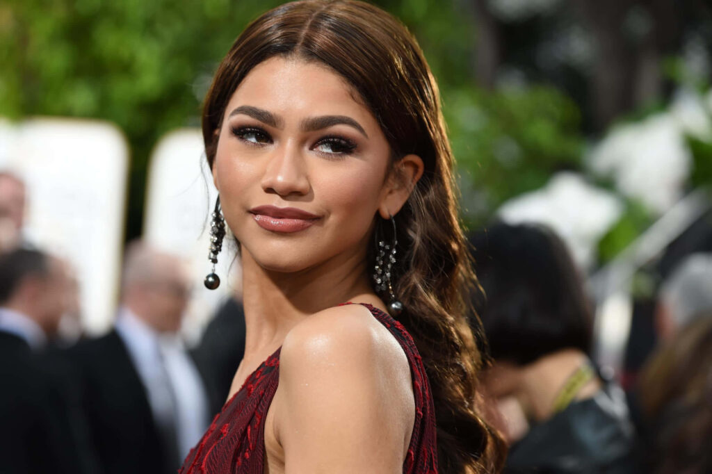Zendaya posing elegantly at outdoor event with glamorous makeup wavy hair and stylish earrings Wallpaper