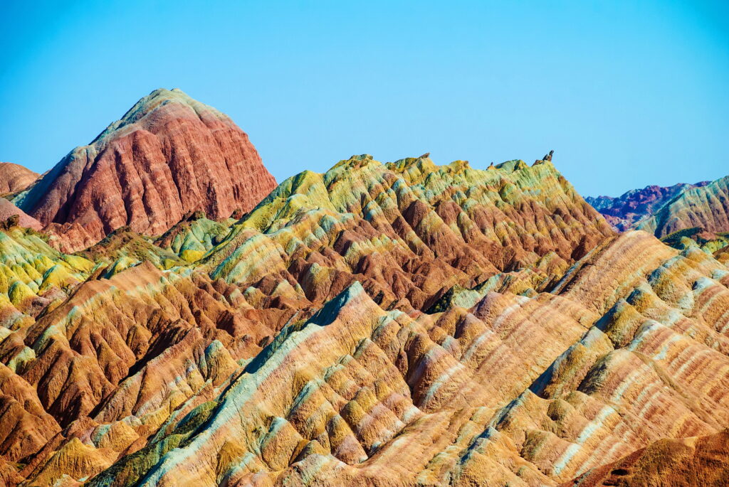 Zhangye Danxia mountains vibrant layered red orange yellow green hues under clear blue sky wallpaper