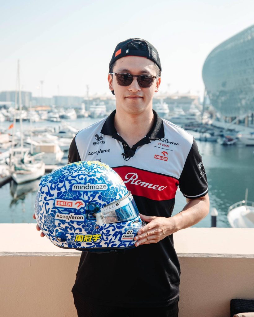F1 driver Zhou Guanyu in Alfa Romeo polo holding blue white porcelain helmet by marina sunlight Wallpaper