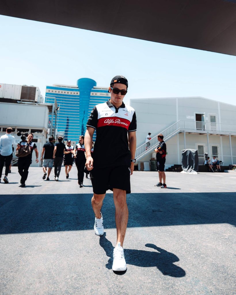 Formula 1 driver Zhou Guanyu in Alfa Romeo polo walking confidently in sunlit paddock wallpaper