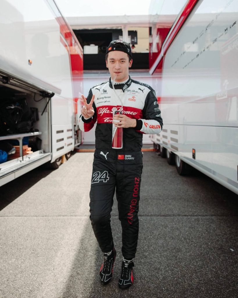 Formula 1 driver Zhou Guanyu in Alfa Romeo suit with number 24 flashing peace sign in paddock Wallpaper