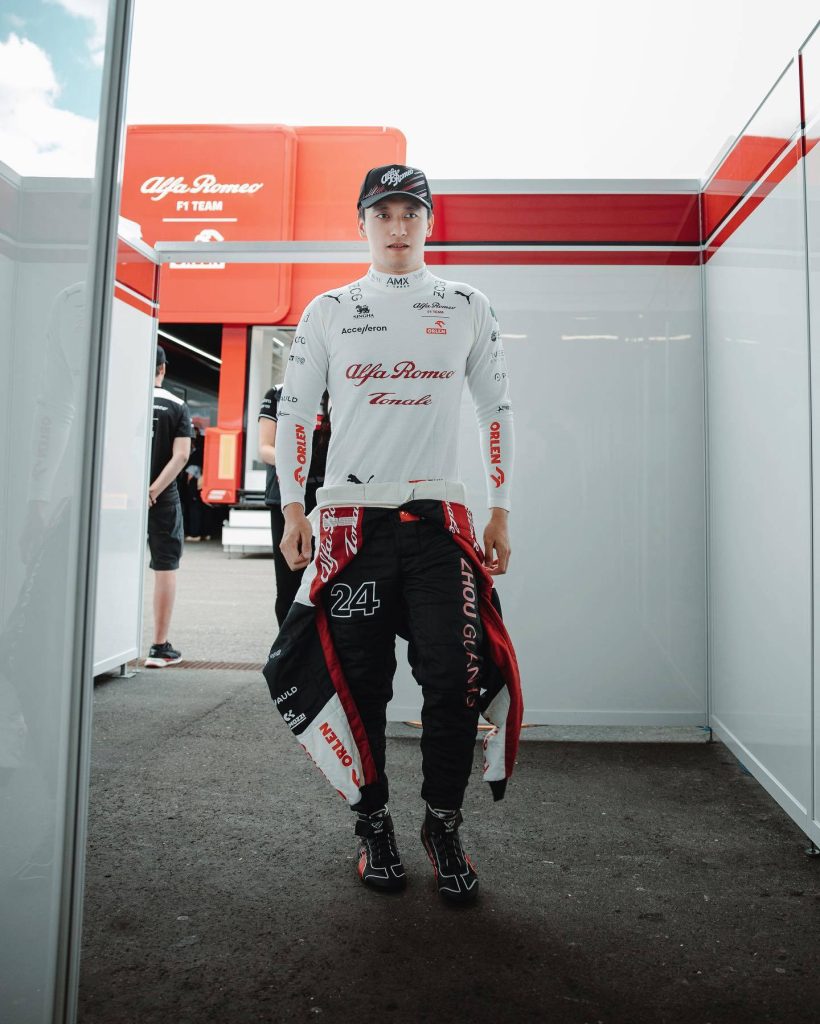 Formula 1 driver Zhou Guanyu in Alfa Romeo racing suit standing confidently in team garage Wallpaper