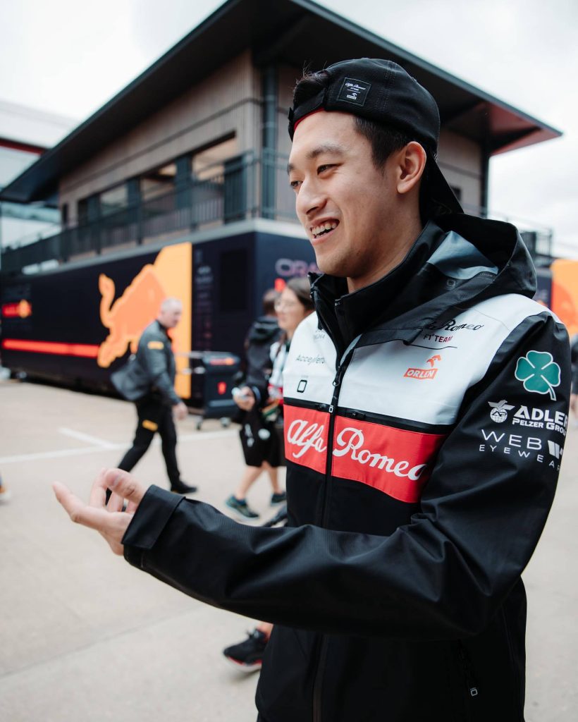 Formula 1 driver Zhou Guanyu in Alfa Romeo team jacket with sponsor logos in paddock background Wallpaper