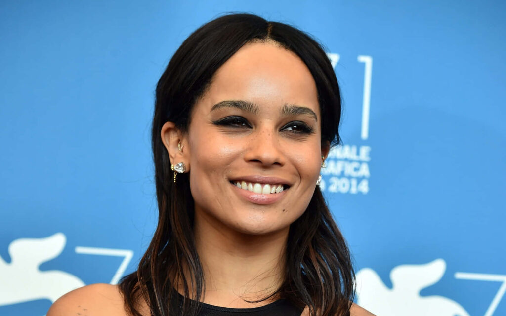 Zoe Kravitz smiling brightly against vivid blue backdrop creating lively radiant wallpaper background