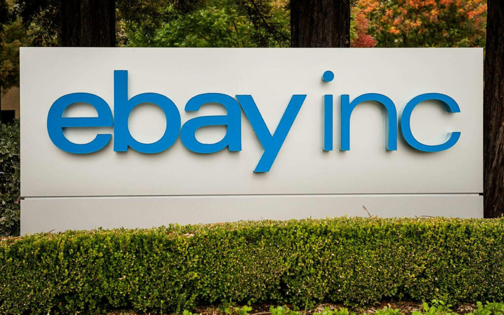 eBay Inc logo in bold blue on white sign with vibrant green trees corporate wallpaper background