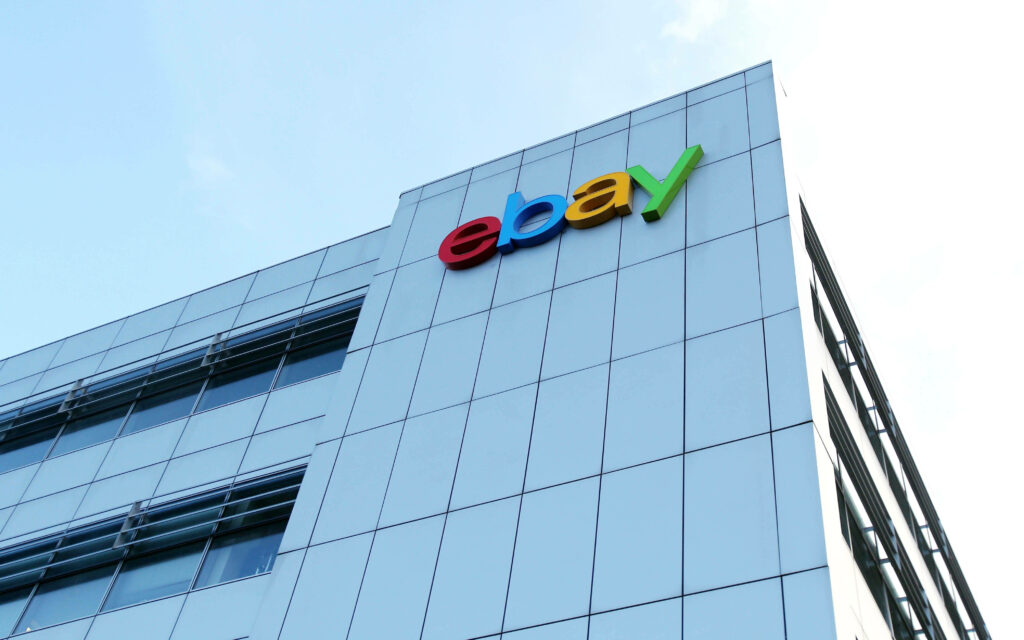eBay logo in vibrant colors on modern glass building facade under clear blue sky wallpaper background