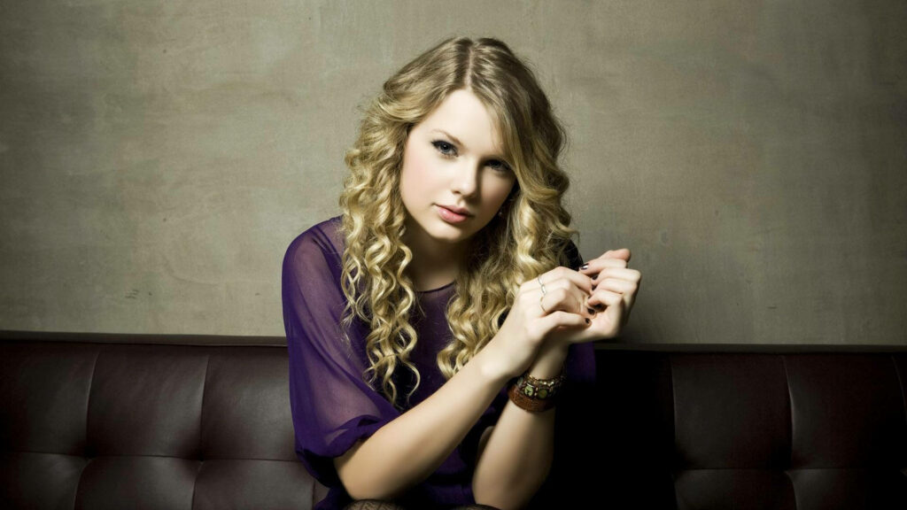Taylor Swift in Purple Sitting on Sofa Posing for a Camera Wallpaper