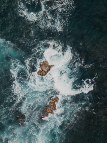 Aerial view of turquoise ocean waves crashing on rugged rocks showcasing dynamic natural textures Wallpaper